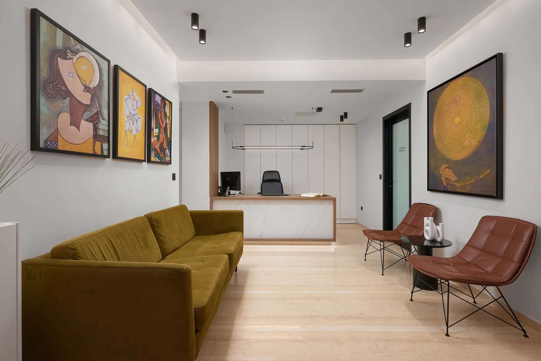 Χώρος υποδοχής με τριθέσιο καναπέ στα αριστερά, δύο μονοθέσιες καρέκλες δεξιά και πίνακες στους τοίχους