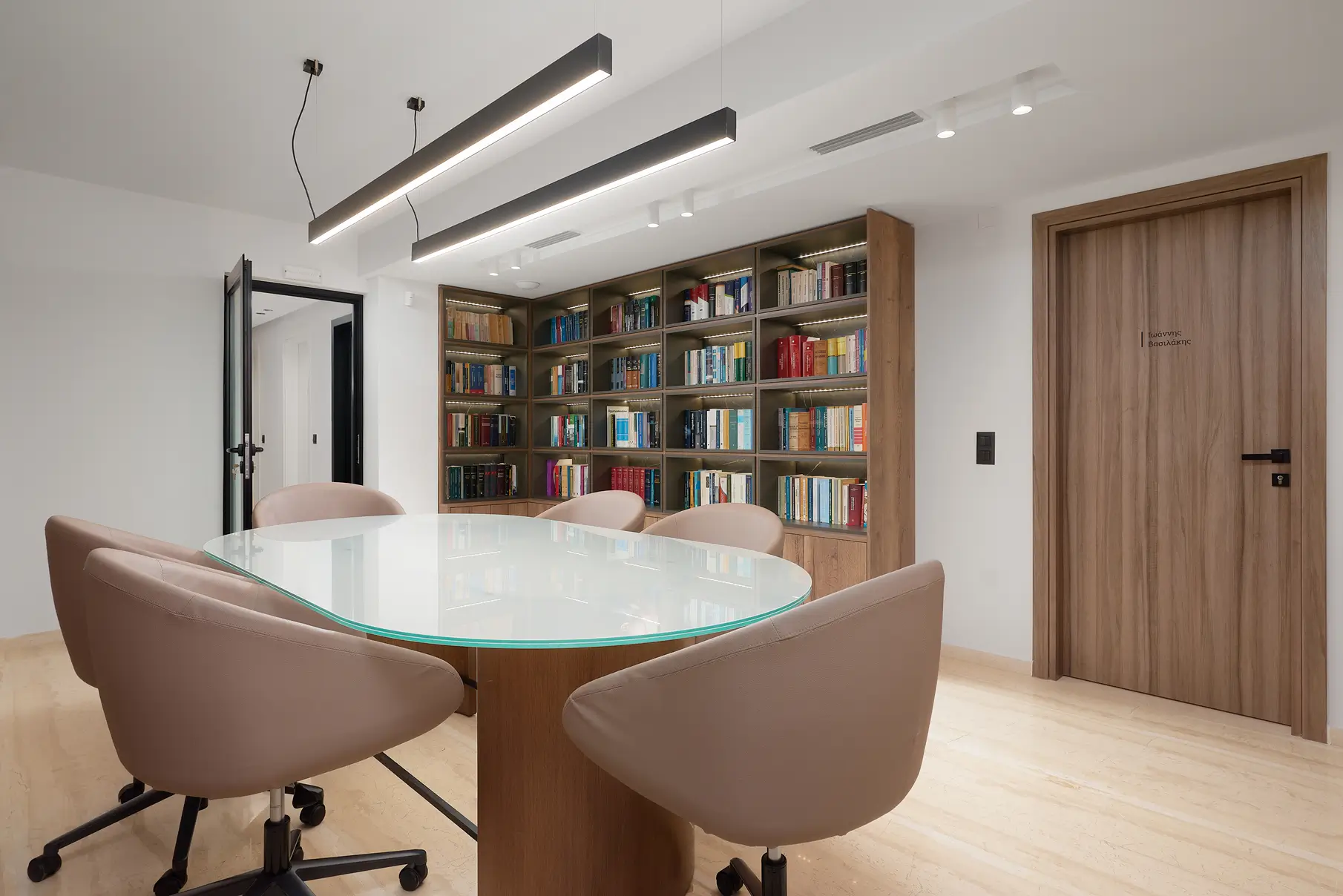 Άποψη της πόρτας που οδηγεί στο γραφείο του δικηγόρου Βασιλάκη Ιωάννη, με την αίθουσα συσκέψεων μπροστά και επιτοίχια βιβλιοθήκη στο φόντο.